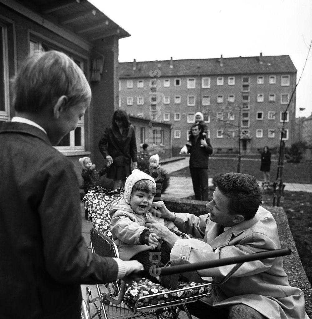 GDR picture archive: Berlin - Eltern holen ihre Kinder vom Kindergarten ab. Ein Vater hockt neben seiner Tochter im Kinderwagen, daneben steht der große Bruder.