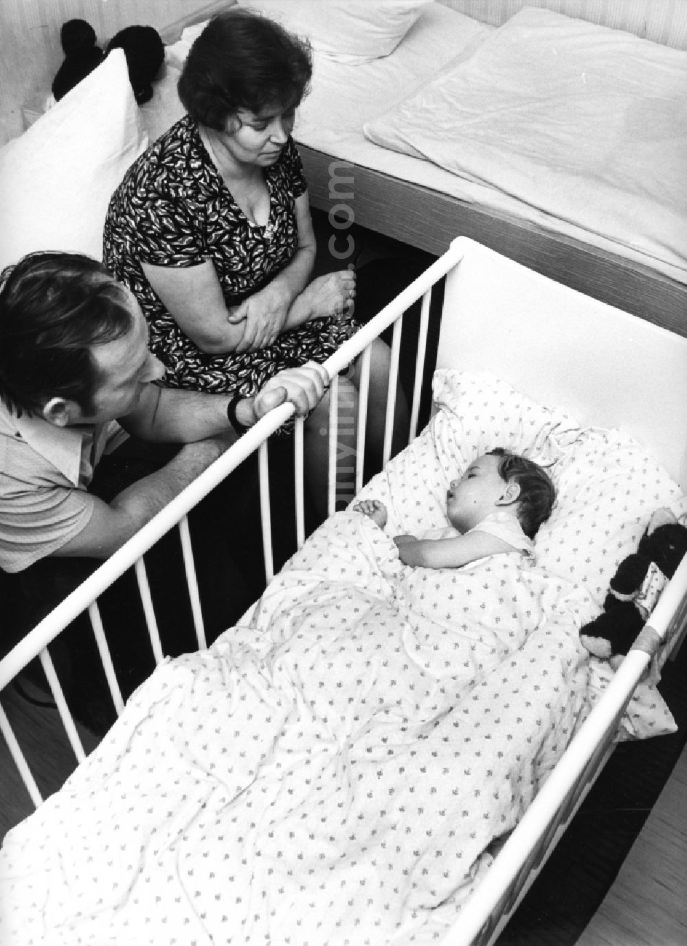 Boxberg/Oberlausitz: Parents sit in the cot of her sleeping child in Boxberg/Oberlausitz in the state Saxony on the territory of the former GDR, German Democratic Republic