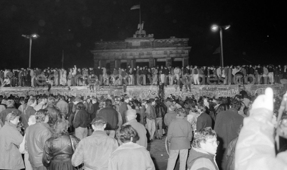 GDR picture archive: Berlin - Passers-by and citizens of both parts of the city peacefully conquer the fortifications and border security structures in front of the Brandenburg Gate in the district of Mitte in Berlin East Berlin on the territory of the former GDR, German Democratic Republic