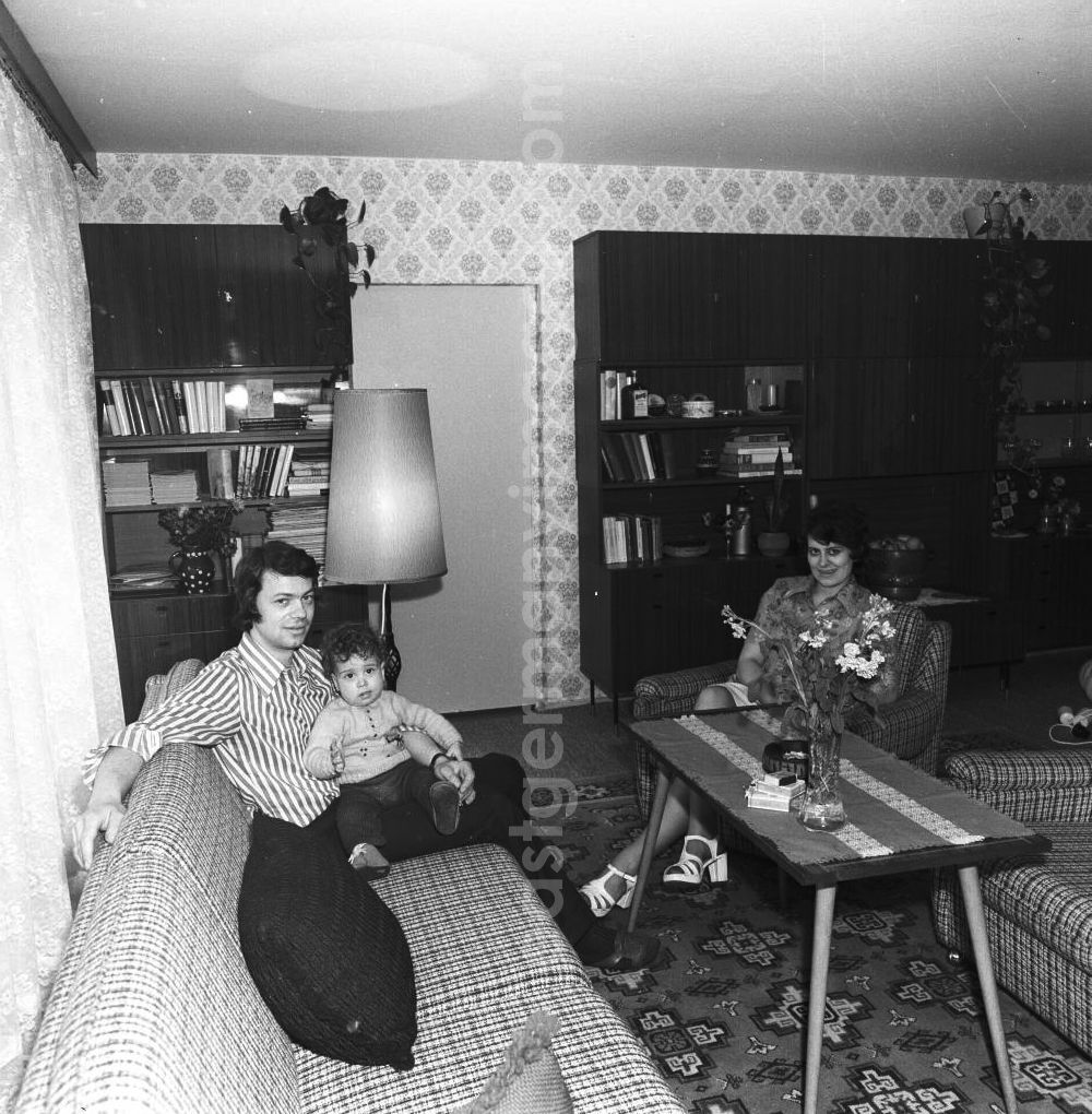 GDR image archive: Fürstenwalde - Wohnzimmer in der Neubauwohnung einer jungen Familie im Stil der siebziger Jahre. Im Hintergrund Schrankwand Typ Hellerau. Paar mit Kind auf dem Sofa / der Couch.