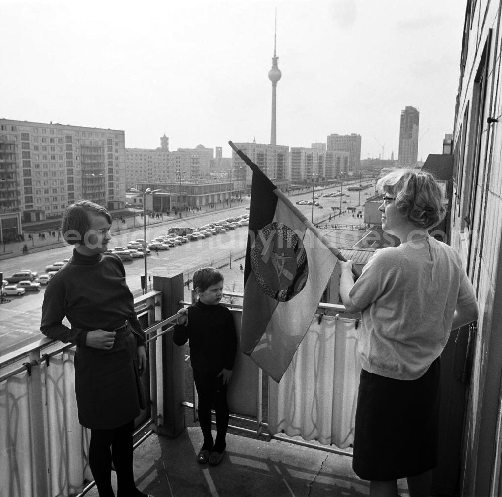 GDR image archive: Berlin - An einem Neubaublock an der Karl-Marx-Allee, der Pracht- und Paradestraße von Berlin (Ost), wird auf dem Balkon der Familie von Susanne Jessen die DDR-Fahne zum 1. Mai aufgehängt. Die Menschen, die hier zu DDR-Zeiten mit Blick auf den Alexanderplatz (Hintergrund) wohnten, gehörten zur privilegierten Schicht bzw. waren angesehene Arbeiter. An den Feiertagen, wie 1. Mai oder 7.Oktober, wurde unten auf der achtspurigen Straße die Tribüne für die Partei- und Staatsführung aufgebaut, auf der die Politiker dann huldvoll die vorbeiziehenden Werktätigen begrüßten.