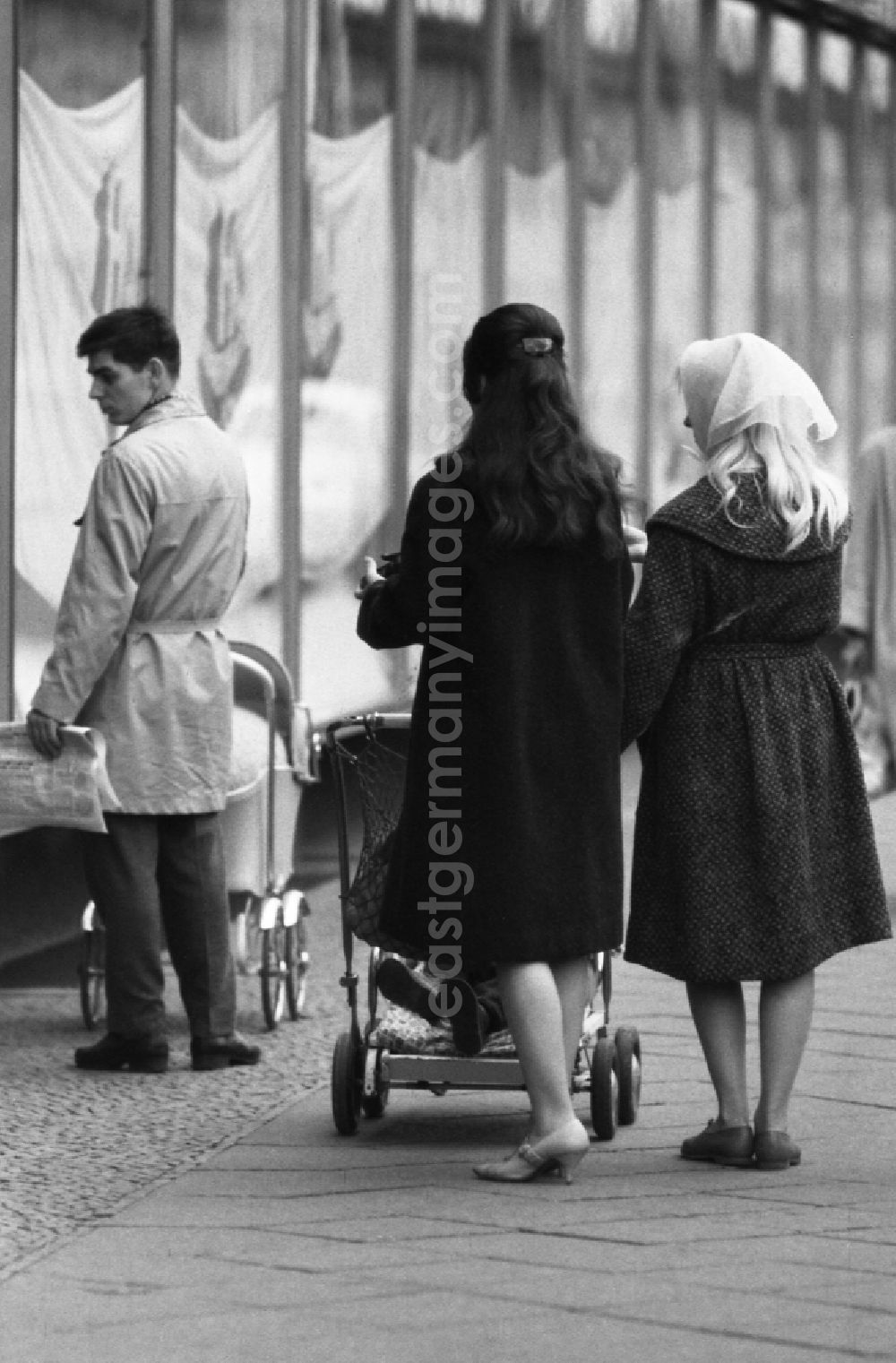 GDR picture archive: Berlin - Man and women with strollers stroll past shop windows in East Berlin in the territory of the former GDR, German Democratic Republic
