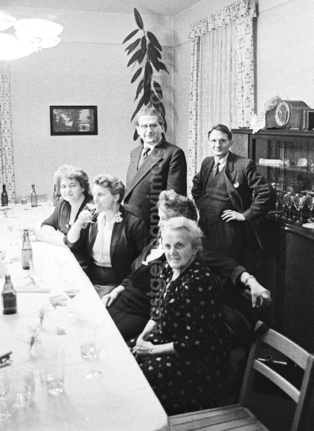 GDR picture archive: Leipzig - Auf einer Familienfeier, drei Frauen und eine ältere Frau an einem Tisch mit Gläsern und Getränken. Stehend, zwei Männer vor einer Anrichte. Bestmögliche Qualität nach Vorlage!