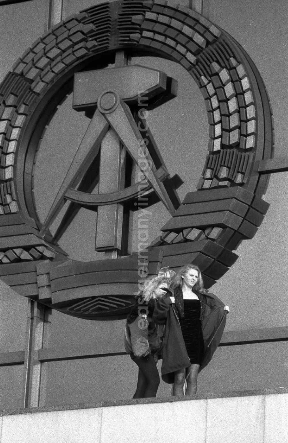 GDR photo archive: Berlin - As a young woman, Anja Kossak presents the latest women's fashion collection at a Playmate photo shoot in front of the entrance area of the Palace of the Republic in the district Mitte in Berlin, which is decorated with the national coat of arms. East Berlin on the territory of the former GDR, German Democratic Republic