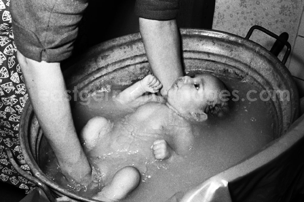 Merseburg: A woman in smock apron bathes a baby in a zinc tub in Merseburg in the federal state Saxony-Anhalt in the area of the former GDR, German democratic republic