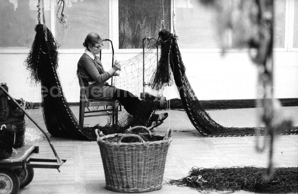 Rostock: A woman sits on a chair and repairs Fichernetze with a net needle in Rostock in the federal state Mecklenburg-West Pomerania in the area of the former GDR, German democratic republic