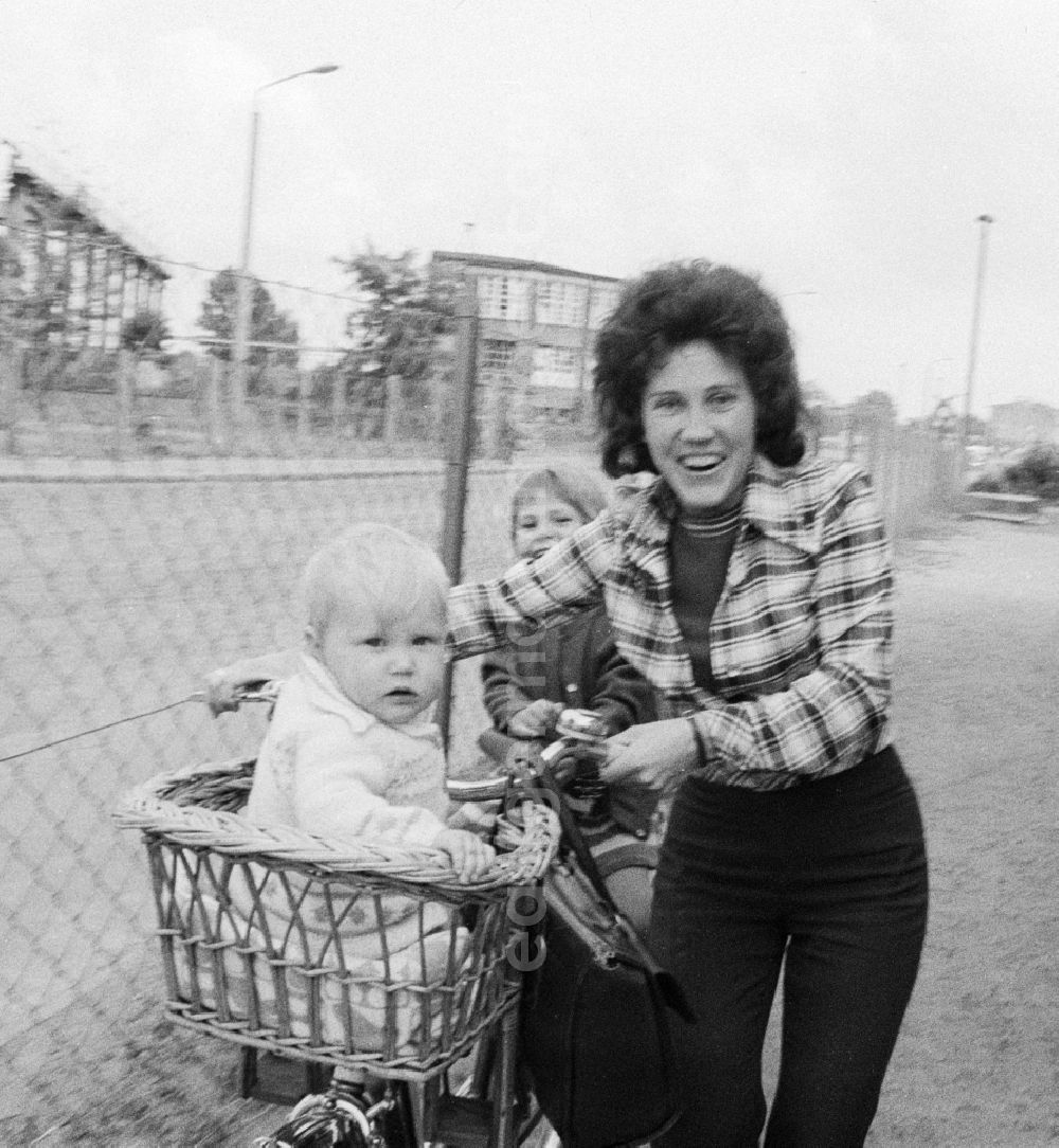 GDR image archive: Eberswalde - A woman with two children and bicycle in Eberswalde in Brandenburg on the territory of the former GDR, German Democratic Republic. A toddler sitting in a bicycle basket willow rods and the other on the carrier from the bike