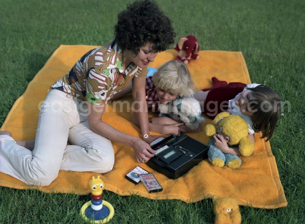 Berlin: Young woman with child spends camping time in the park Monbijoupark on a blanket with a radio recorder Anett IS of the VEB RFT Sternradio Berlin in the Mitte district of Berlin, the former capital of the GDR, German Democratic Republic