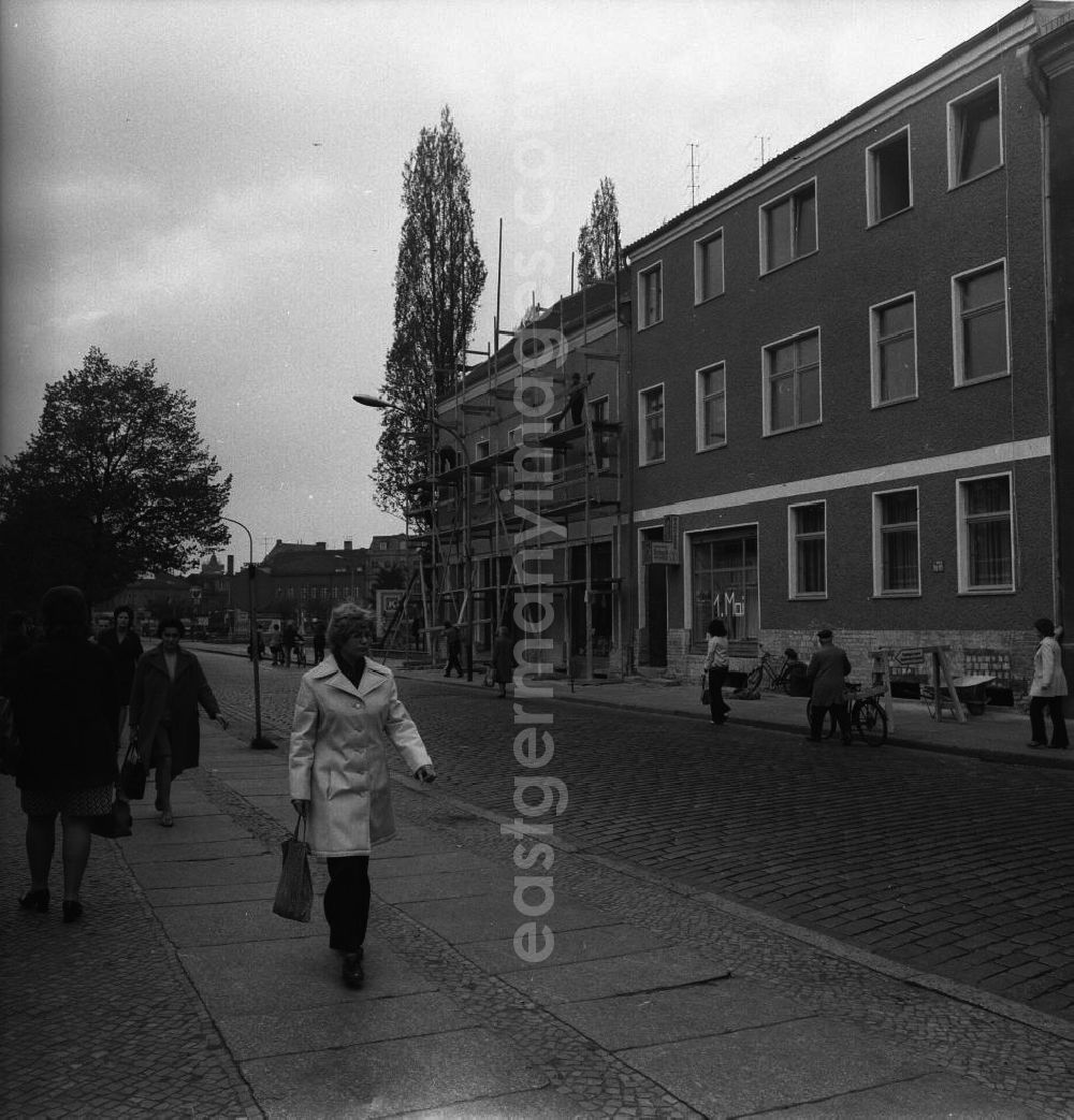 GDR photo archive: Fürstenwalde - Alltagsszene / Stadtansicht. Fußgänger auf Bürgersteig und Straße, einige schieben ihre Fahrräder. Bauarbeiter demontieren ein Baugerüst.