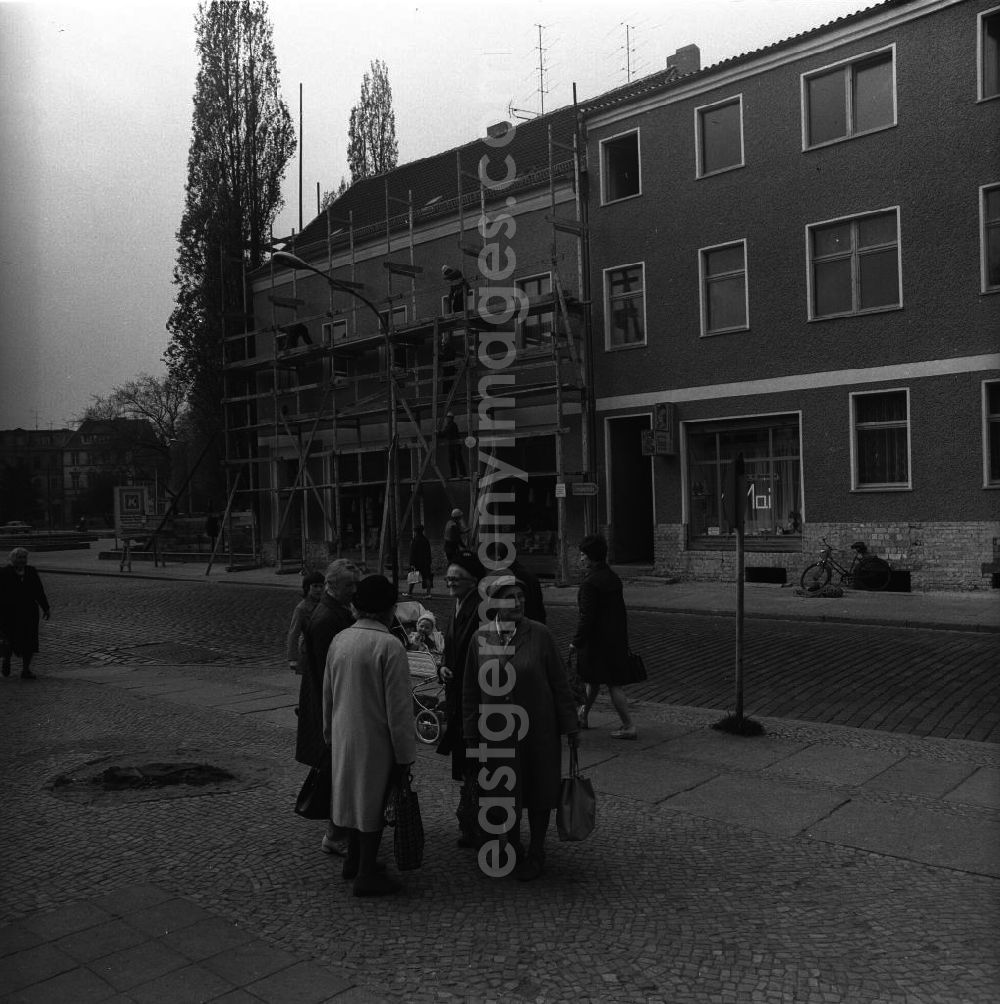 GDR picture archive: Fürstenwalde - Gruppe älterer Damen führt eine Unterhaltung auf dem Bürgersteig. Passanten nähern sich der Gruppe, gehen an ihr vorbei und überqueren die Straße. Im Hintergrund bauen Arbeiter ein Gerüst ab.