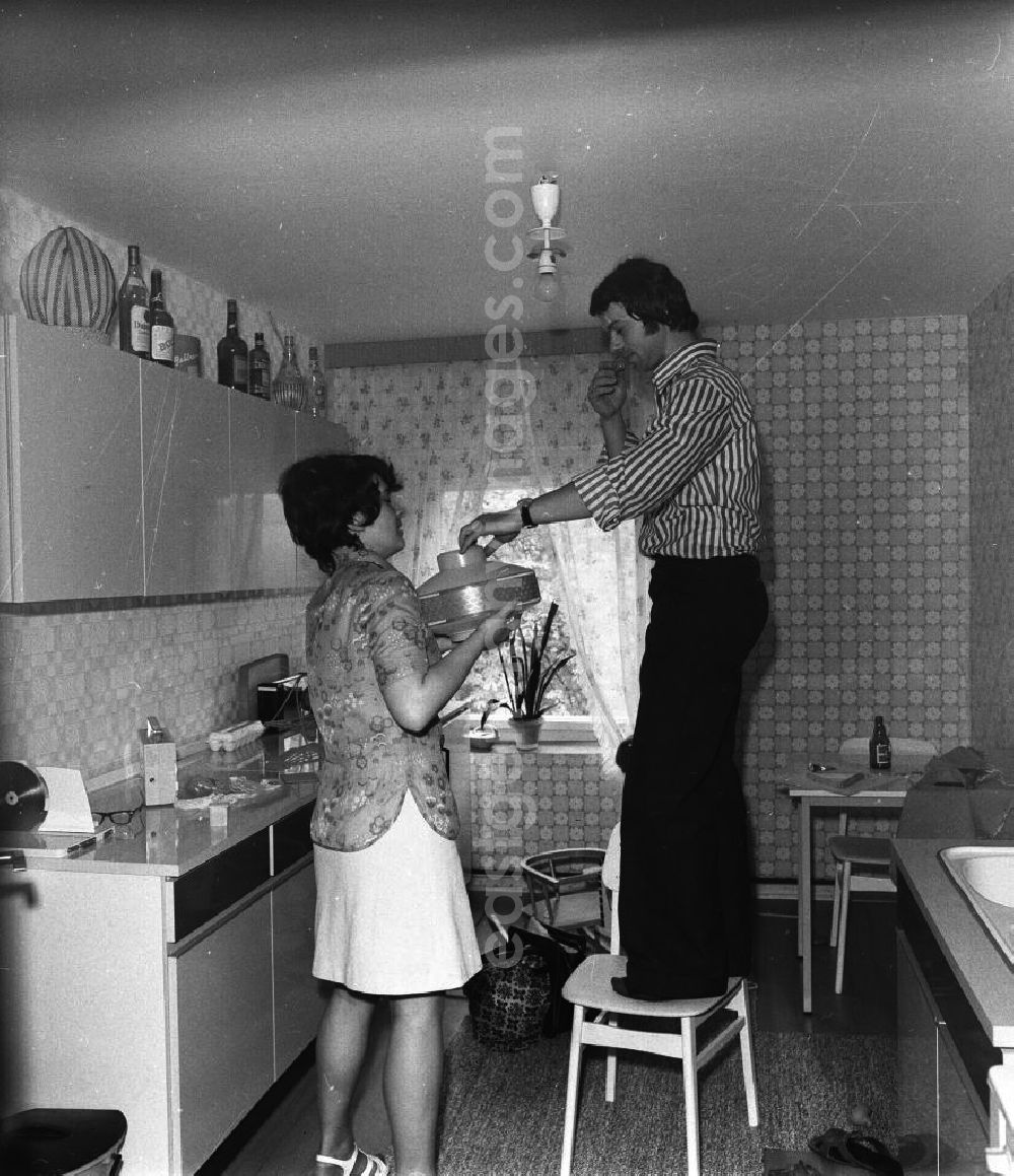 Fürstenwalde: Küche in der Neubauwohnung einer jungen Familie im Stil der siebziger Jahre. Ein junges Paar wechselt die Glühbirne der Küchen-Leuchte.
