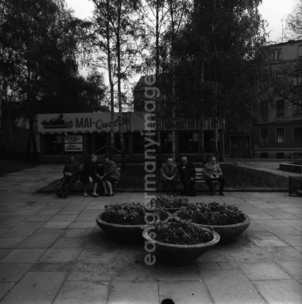 GDR picture archive: Fürstenwalde - Senioren sitzen auf Bänken an einer Grünfläche vor einer Imbissbude / Geschäft Mai-Quelle.