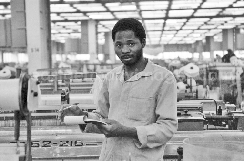 GDR photo archive: Ebersbach - Guest worker man (as part of the agreement on the temporary employment of Mozambican workers in socialist companies in the GDR) at the workplace and the factory equipment in the workshop with loom machines in the VEB Lautex spinning mill in Ebersbach in GDR