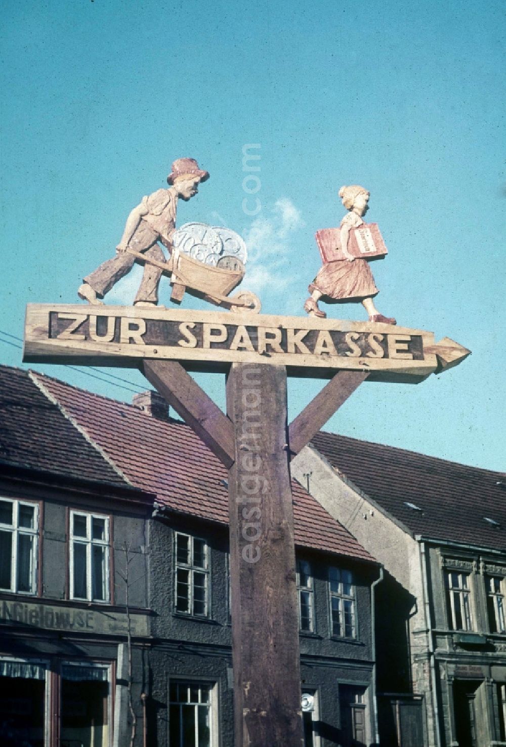 GDR image archive: Neustrelitz - A carved signpost with figures of wood him the way to the savings bank points in Neustrelitz in the federal state Mecklenburg-West Pomerania in the area of the former GDR, German democratic republic