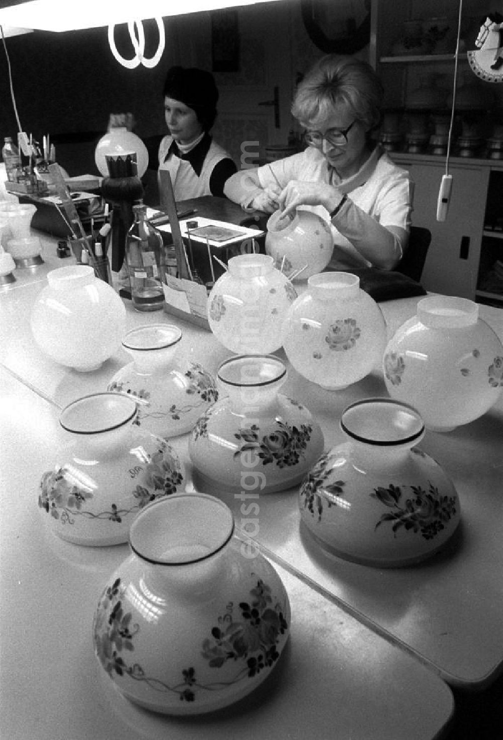 GDR picture archive: Berlin - Glasmalerei / Glasmalerinnen der PGH des Kunsthandwerkes arbeiten in ihrer Werkstätte in der Schreinerstraße 58. Blick über Vasen die zum trocknen zusammen stehen auf die Arbeiterinnen beim verzieren / bemalen von Glasvasen.