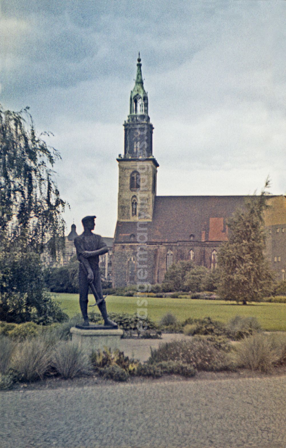 GDR photo archive: Berlin - Sculpture of a construction worker on Rathausstrasse in front of the bell tower of the sacred building of the church St. Marienkirche on Karl-Liebknecht-Strasse in the Mitte district of Berlin East Berlin on the territory of the former GDR, German Democratic Republic
