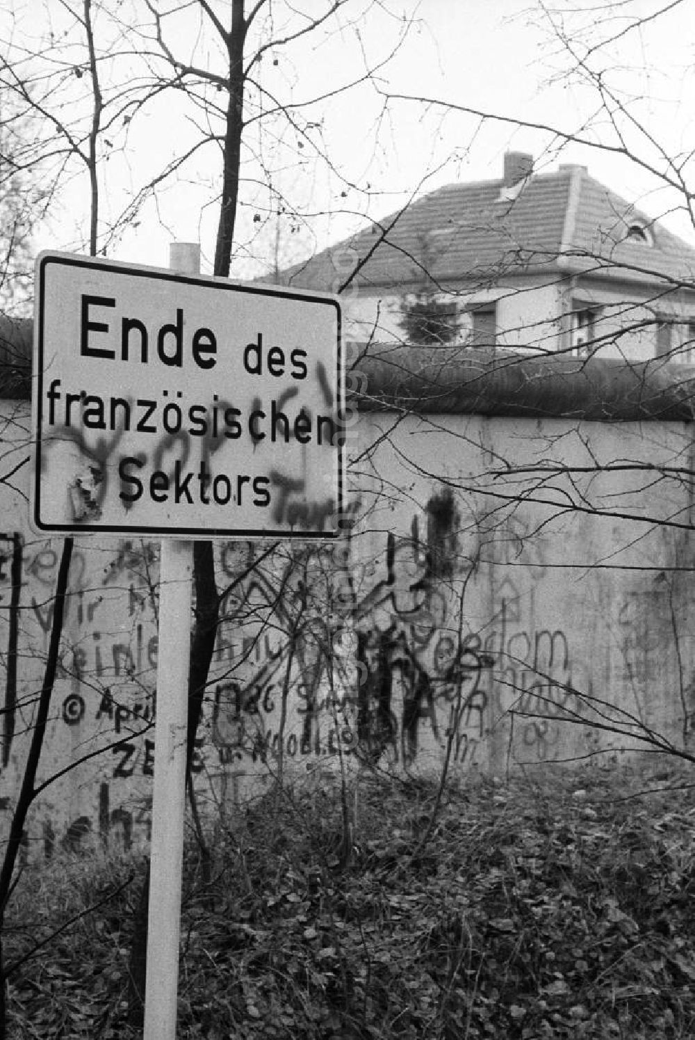 Hohen Neundorf: Schild vor der Grenze / Mauer der DDR mit der Aufschrift Ende des französischen Sektors. Mauer und Schild mit Graffiti / Schmierereien, dahinter ein Dach eines Einfamilienhauses.