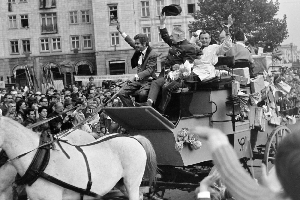 GDR photo archive: Berlin - Participants of the May 1st parade on the streets of the city center at Strausberger Platz stand in front of a historic stagecoach with the actors Heinz Fuelfe (speed illustrator Taddeus Punkt), Eckart Friedrichson (Master Needle Eye), Heino Winkler (Master Stamp) from the GDR children's television in Berlin East Berlin in the territory of the former GDR, German Democratic Republic