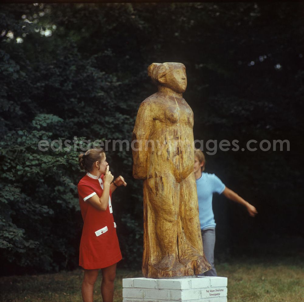 GDR image archive: Berlin - Junges Pärchen in einem Berliner Park neben einer Holzskulptur Schweigsame des Bildhauers Prof. Adam Smolana (1921-1987). Jung couple in a park beside a wood sculpture of the carver Adam Smolana.