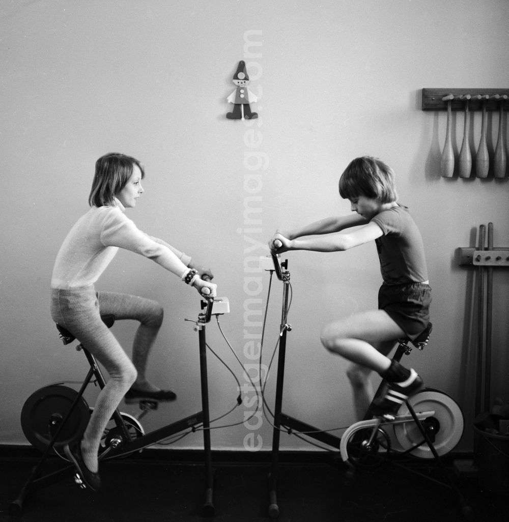 GDR image archive: Berlin - 2 children exercising on exercise bikes fitness and stamina in the Children's Clinic in Klinikum Berlin-Buch in Berlin, the former capital of the GDR, the German Democratic Republic. A mother sitting with her baby sits treatment rooms