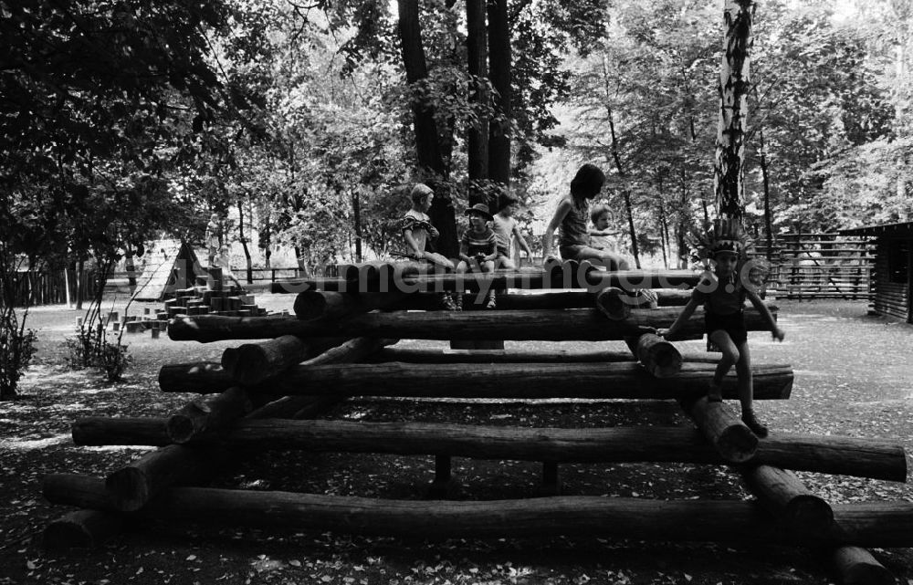 GDR picture archive: Berlin - Kinder spielen auf dem Indianerspielplatz / Abenteuerspielplatz im Biesdorfer Park in Berlin-Lichtenberg. Ein Kind trägt Indianerschmuck auf dem Kopf.