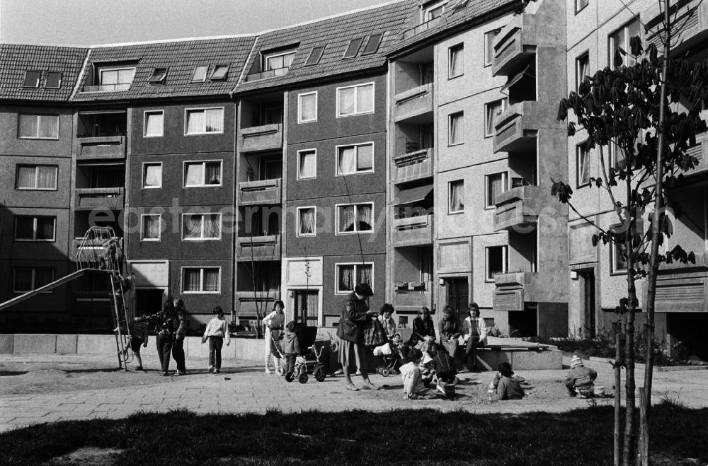 GDR photo archive: Erfurt - Blick in den Innenhof eines Neubaugebietes mit Plattenbauten im Hintergrund. Eltern mit ihren Kindern spielen zusammen auf dem Spielplatz.