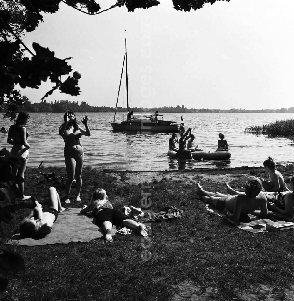 GDR picture archive: Berlin - Jugendliche an der Badestelle auf dem Internationalen Campingplatz (Intercamping) bei Schmöckwitz in Berlin-Köpenick am Ufer des Krossinsee. Ein Segelboot ist im Hintergrund auf dem See.