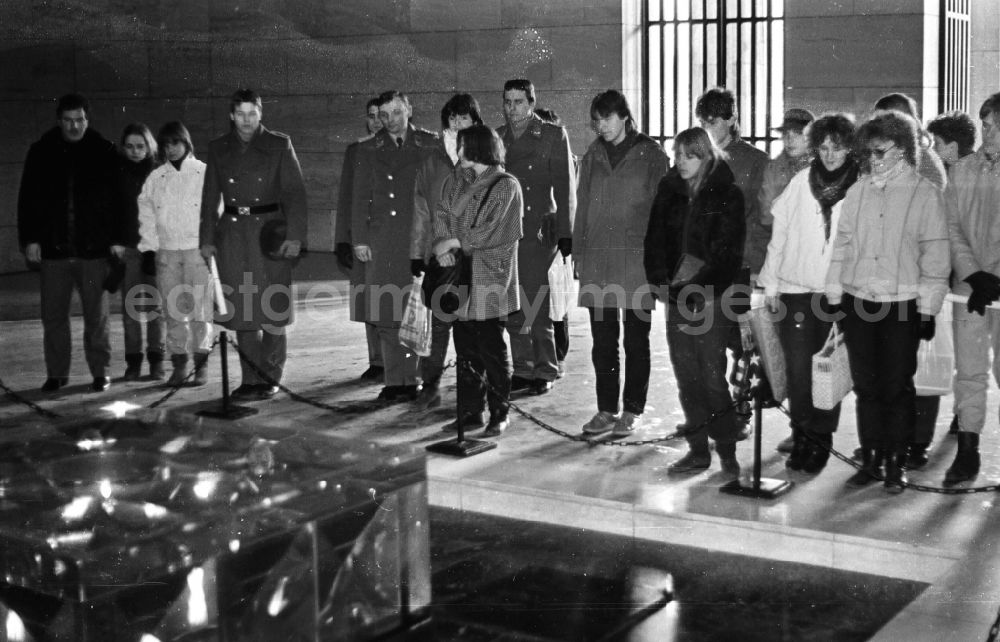 GDR photo archive: Berlin - Joint visit by soldiers and army members of the NVA fighter squadron Heinrich Rau and young people from a civilian mentor brigade in front of the Eternal Flame in the national memorial against the victims of war and fascism in Schinkel's Neue Wache on the boulevard Unter den Linden in the Mitte district in Berlin East Berlin on the territory of the former GDR, German Democratic Republic