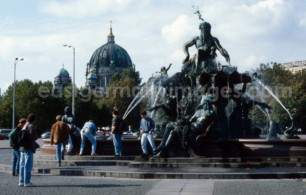 GDR picture archive: Berlin - Mitte - A group of teenagers refreshed on Neptune Fountain in Berlin - Mitte. In the background of the Berlin cathedral is seen. From a basic dish on a three-tier base, the powerful figure of the ancient Roman sea god Neptune rises