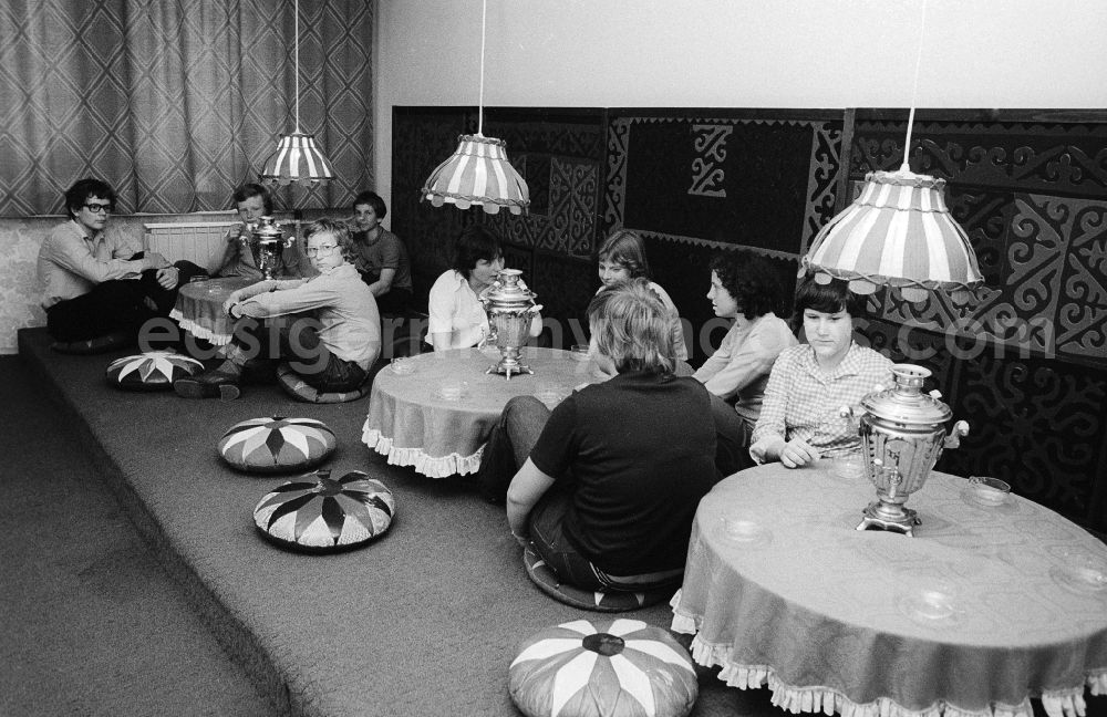 GDR photo archive: Berlin - Youngsters sit on the ground in the tearoom at the youth tourist's hotel Egon Schultz in the animal park in Berlin, the former capital of the GDR, German democratic republic. Samovars with warm tea stand on the tables. Today one says animal park ABACUS hotel