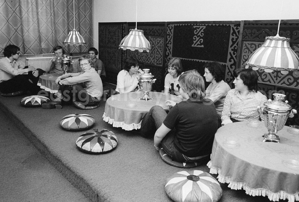 GDR picture archive: Berlin - Youngsters sit on the ground in the tearoom at the youth tourist's hotel Egon Schultz in the animal park in Berlin, the former capital of the GDR, German democratic republic. Samovars with warm tea stand on the tables. Today one says animal park ABACUS hotel