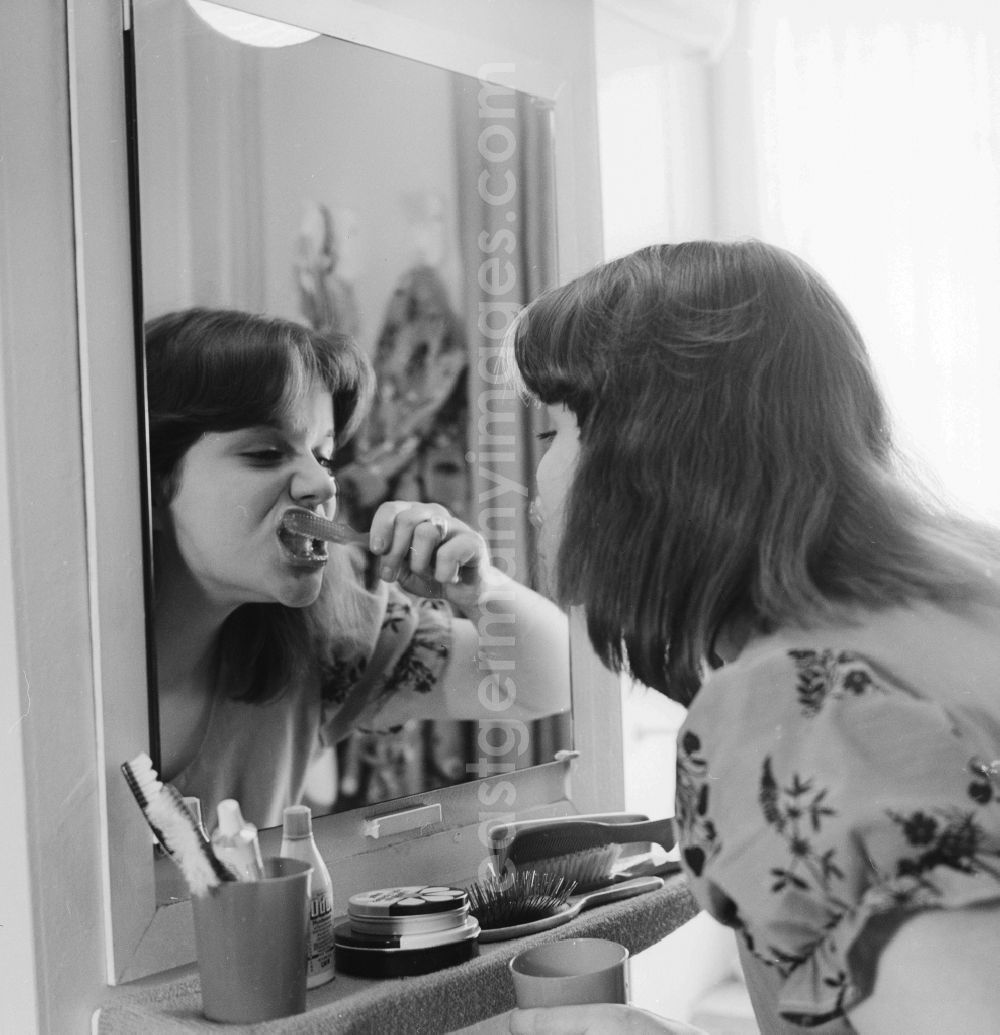GDR photo archive: Berlin - Young woman brushing teeth in front of the mirror in Berlin