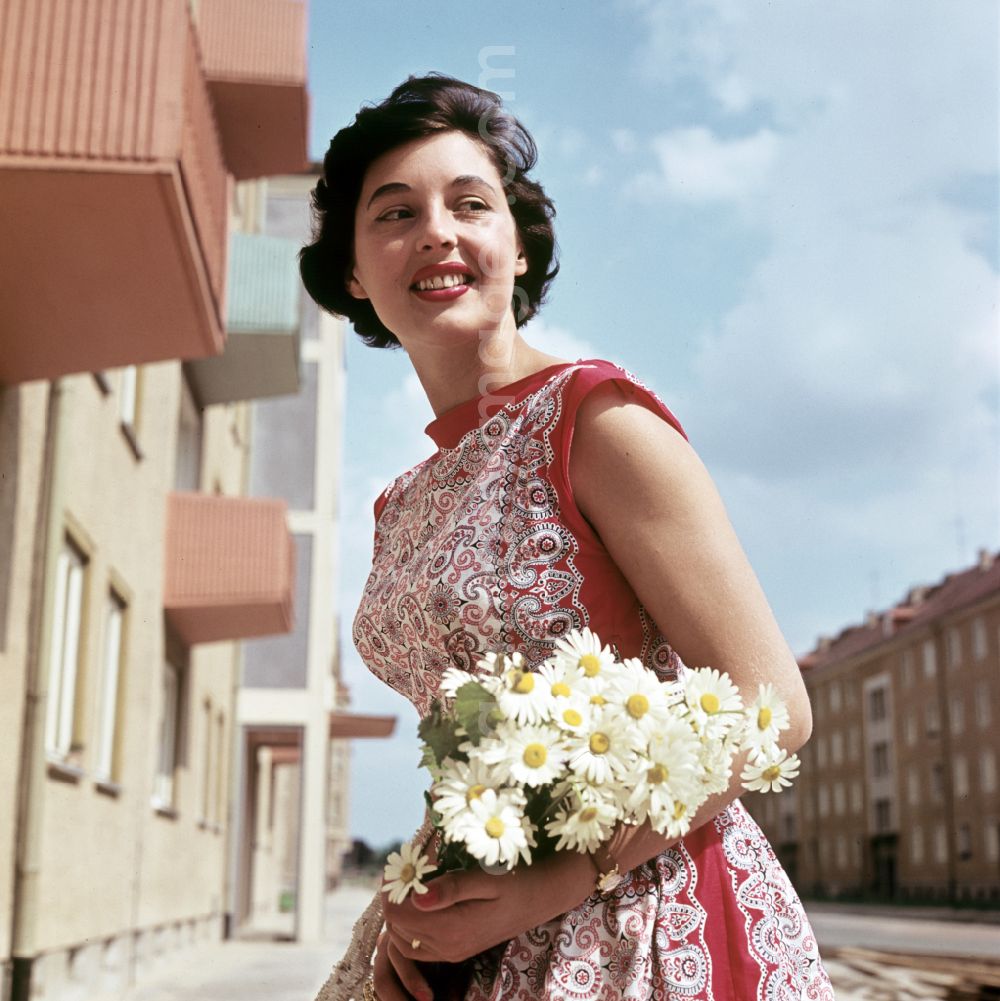 GDR photo archive: Coswig - A young woman poses with flowers in front of a newly built block of flats in Coswig, Saxony in the territory of the former GDR, German Democratic Republic