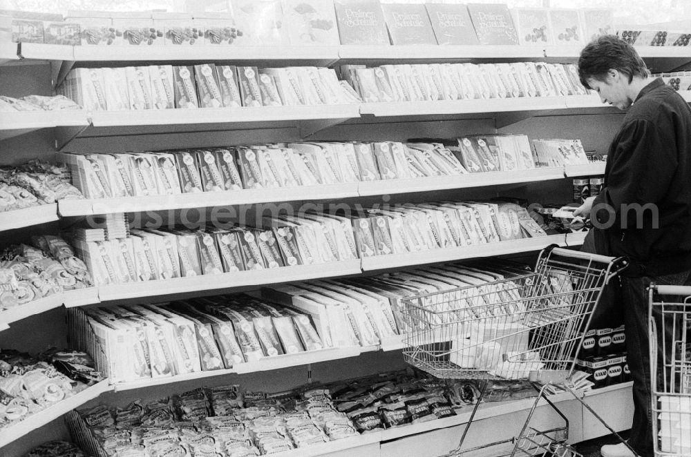 GDR picture archive: Berlin - A young woman stands in front of the candy shelf in a department store in Berlin, the former capital of the GDR, the German Democratic Republic. The shelves are filled partly with Ostprodukten as well with Western products