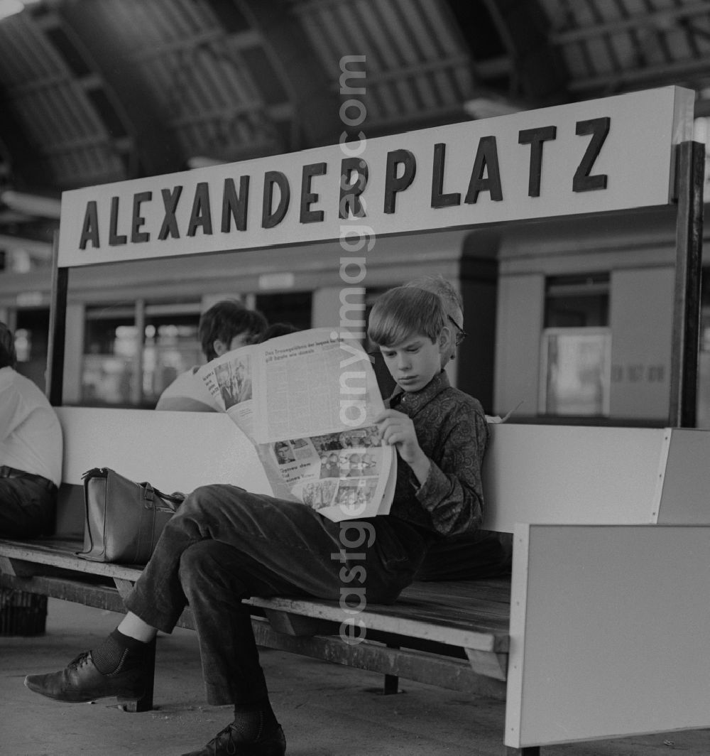 GDR picture archive: Berlin - Mitte - Boy reading a newspaper on a bench in the station Alexanderplatz in Berlin - Mitte