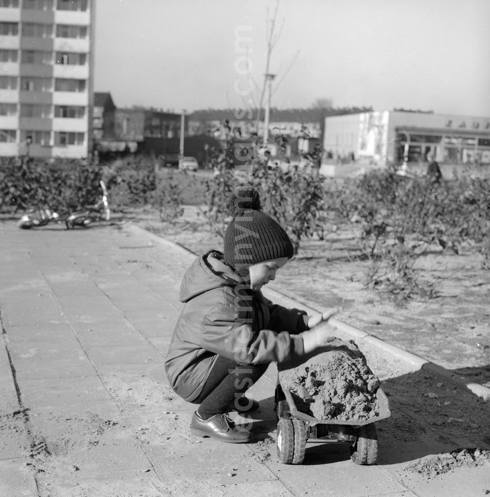 GDR picture archive: Berlin - A little boy in a poodle cap plays with his plastic truck in the sandbox in a courtyard of a residential area in Berlin, the former capital of the GDR, German Democratic Republic