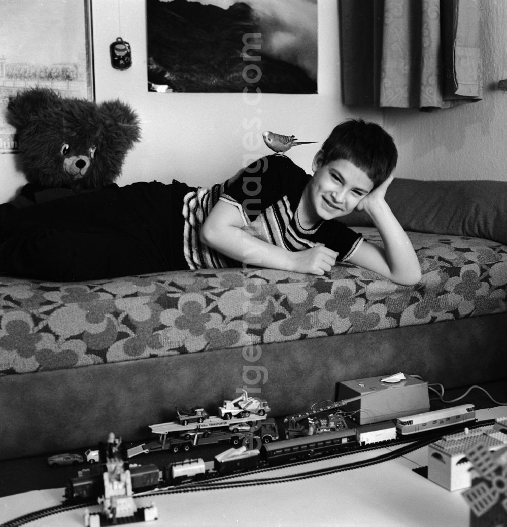 Berlin: A boy playing with his model railway in his nursery in Berlin, the former capital of the GDR, the German Democratic Republic. His pet, a budgie, sitting on his back and looks on