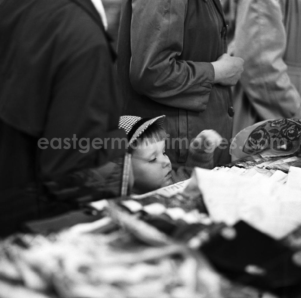 GDR picture archive: Leipzig - Inmitten der Kunden schaut ein kleiner Junge in einem Kaufhaus in Leipzig neugierig auf die Ladentheke.