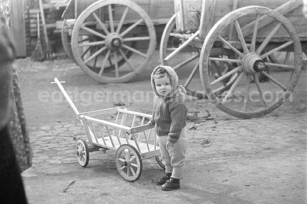 GDR image archive: Markkleeberg - Landleben: Kind mit einem Bollerwagen auf einem Bauernhof. Im Hintergrund ausschnittsweise Wagenräder. Bestmögliche Qualität nach Vorlage!