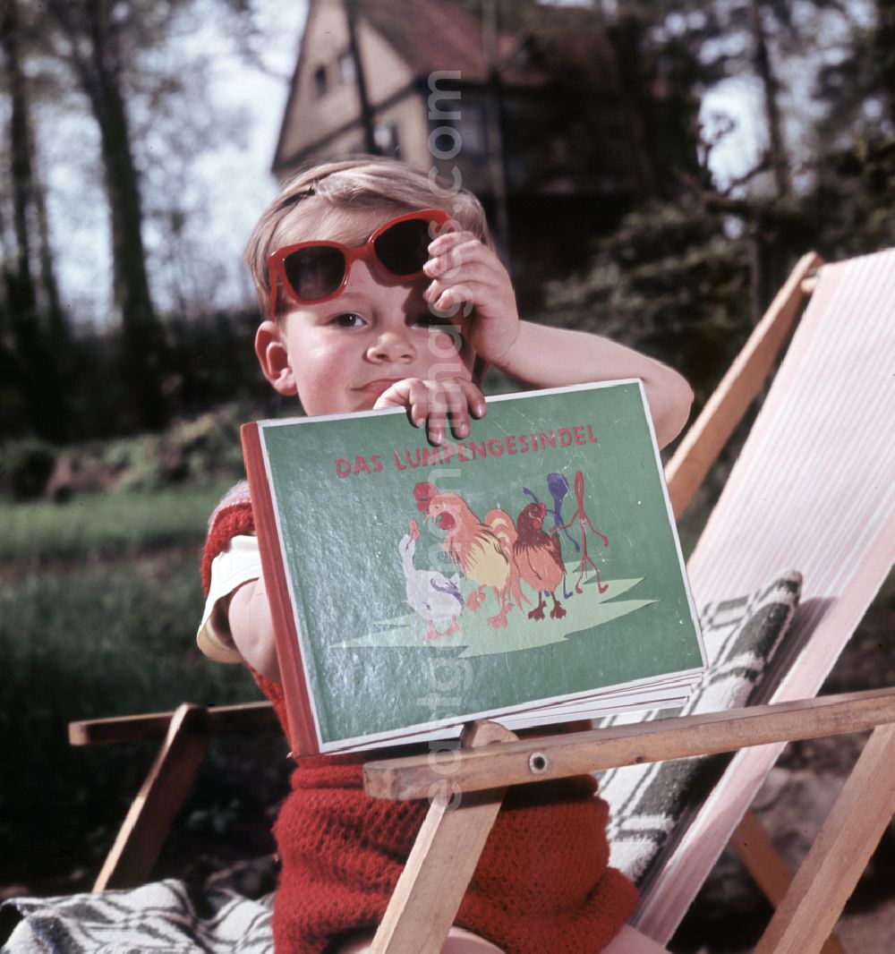 GDR photo archive: Coswig - A boy sits on a deck chair with a book and sunglasses in Coswig, Saxony in the territory of the former GDR, German Democratic Republic