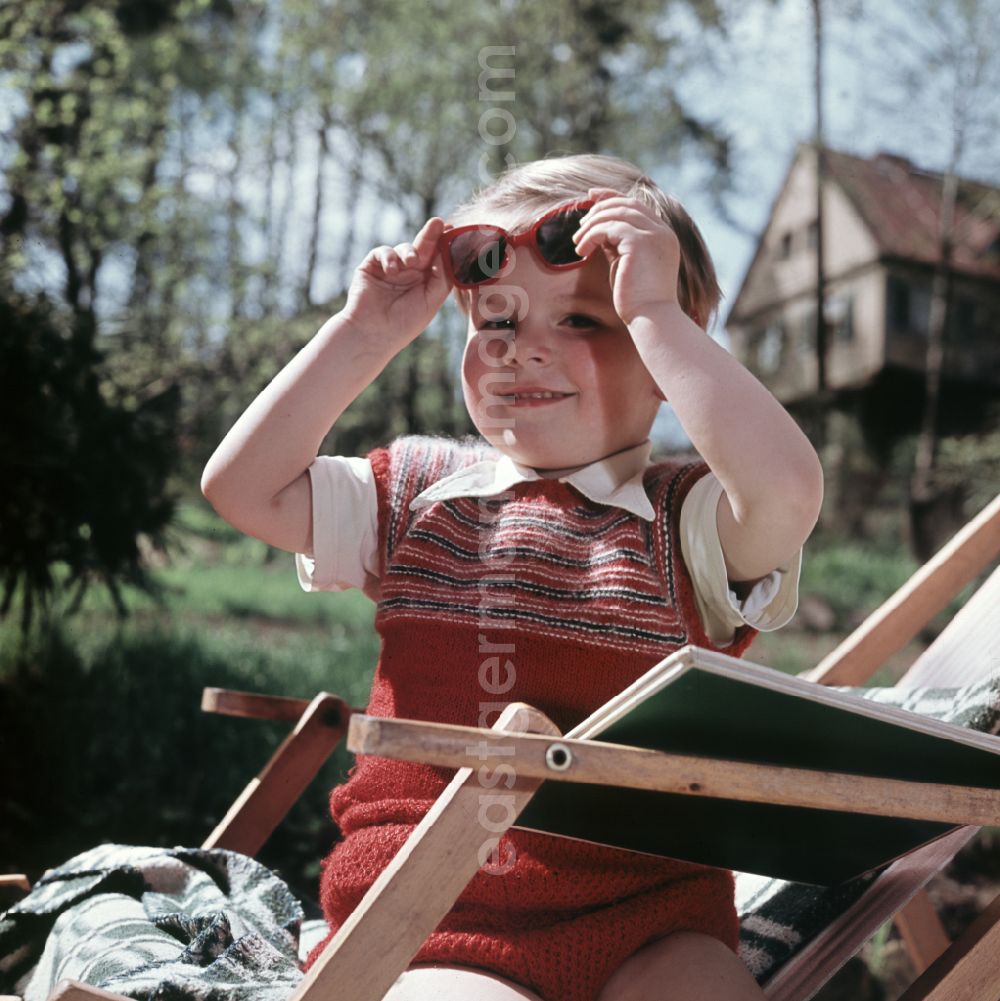 GDR picture archive: Coswig - A boy sits on a deck chair with a book and sunglasses in Coswig, Saxony in the territory of the former GDR, German Democratic Republic