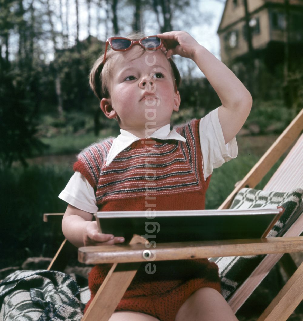 GDR image archive: Coswig - A boy sits on a deck chair with a book and sunglasses in Coswig, Saxony in the territory of the former GDR, German Democratic Republic
