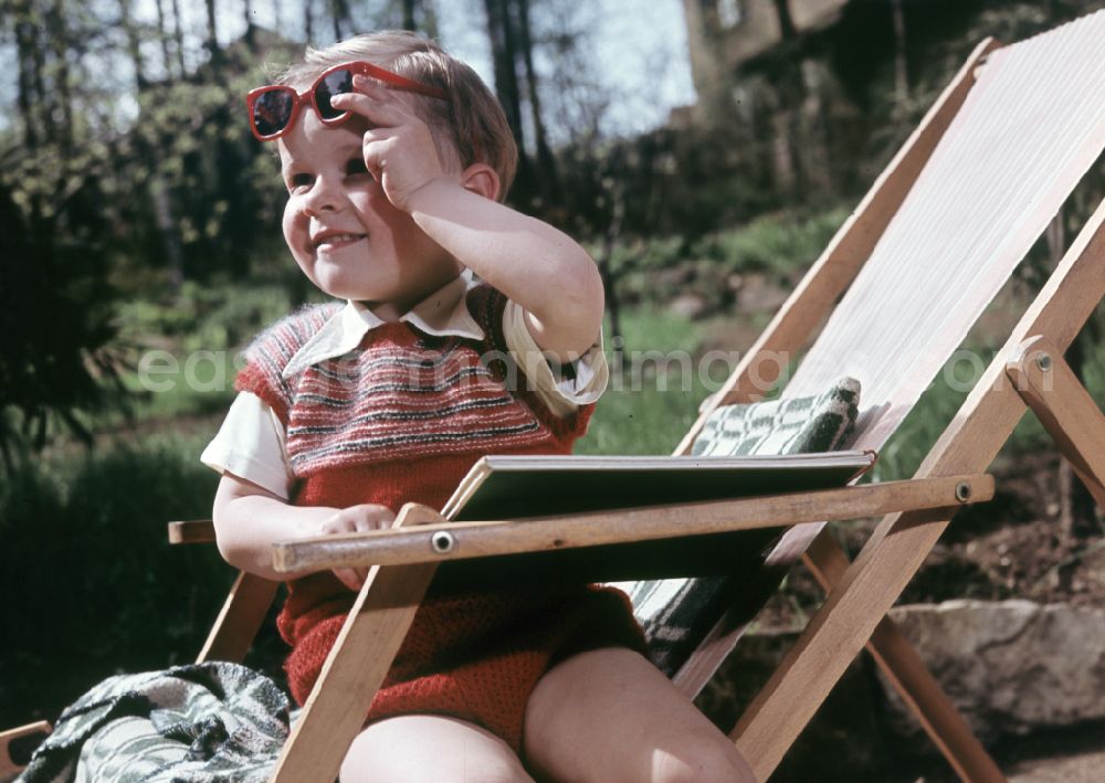 Coswig: A boy sits on a deck chair with a book and sunglasses in Coswig, Saxony in the territory of the former GDR, German Democratic Republic