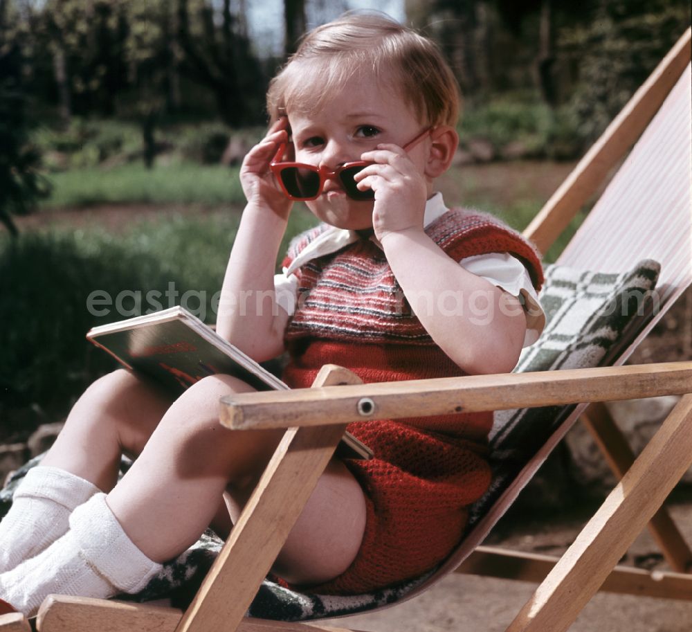 GDR image archive: Coswig - A boy sits on a deck chair with a book and sunglasses in Coswig, Saxony in the territory of the former GDR, German Democratic Republic