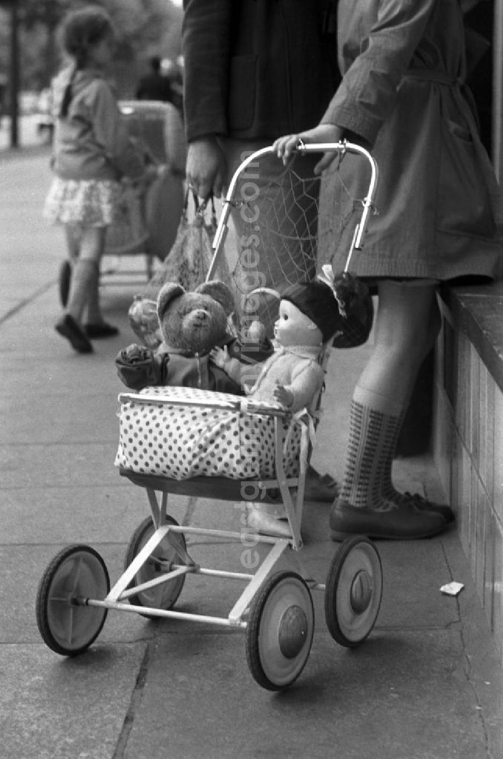 GDR image archive: - Ein Mädchen schaut neugierig durch das Schaufenster eines Dresdner Spielwarengeschäftes, in der Hand ihren Puppenwagen mit Teddy und Püppi.