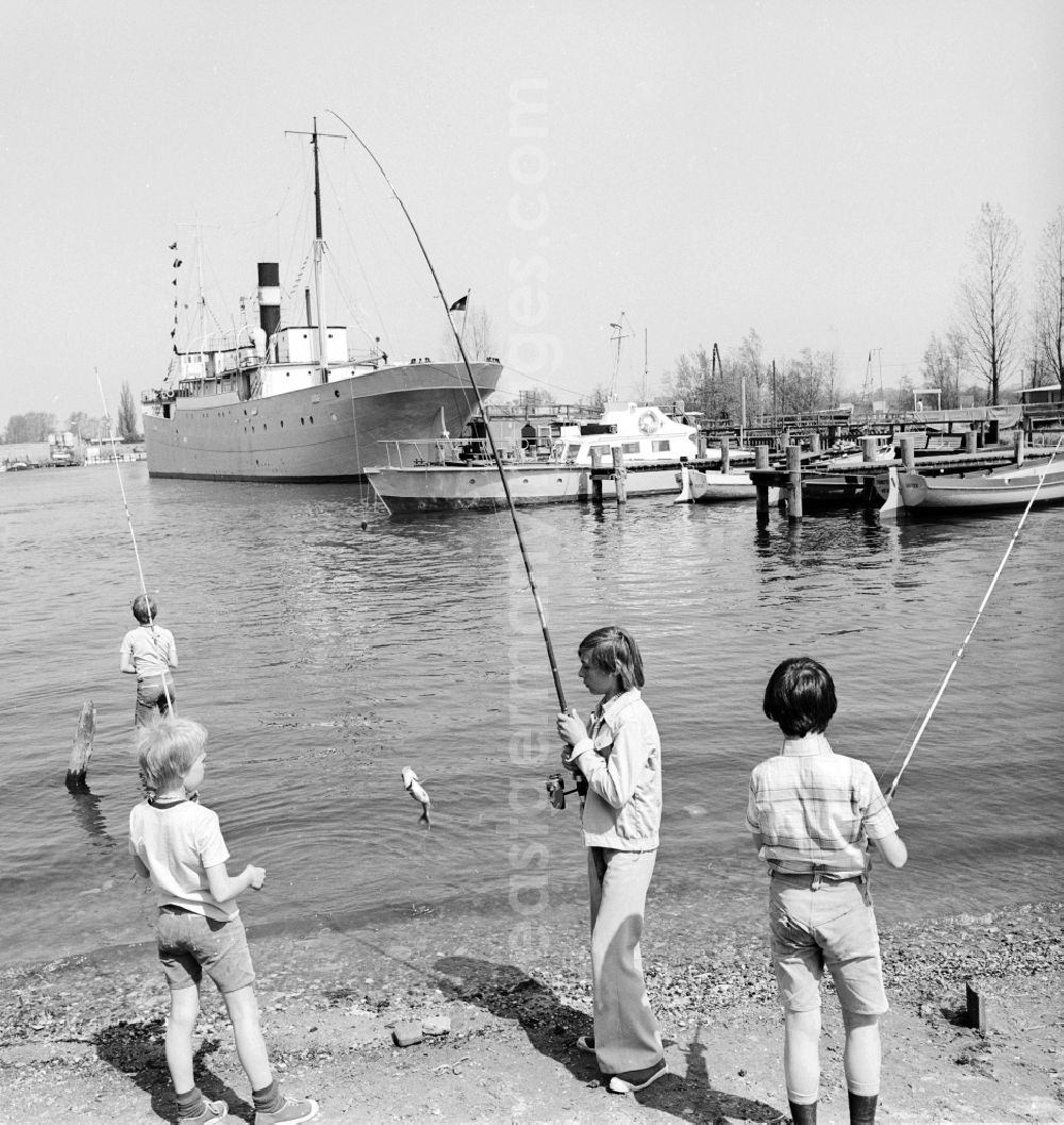 Rostock: Children catch fish on the banks of the lower Warnow in Rostock in Mecklenburg-Vorpommern on the territory of the former GDR, German Democratic Republic. In the background the pioneer ship forward