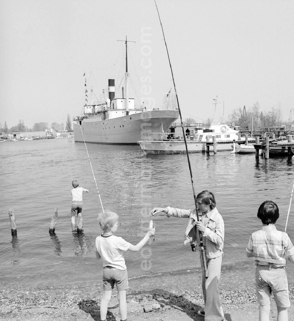 GDR image archive: Rostock - Children catch fish on the banks of the lower Warnow in Rostock in Mecklenburg-Vorpommern on the territory of the former GDR, German Democratic Republic. In the background the pioneer ship forward