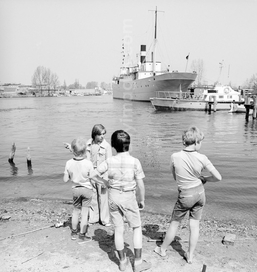 GDR photo archive: Rostock - Children catch fish on the banks of the lower Warnow in Rostock in Mecklenburg-Vorpommern on the territory of the former GDR, German Democratic Republic. In the background the pioneer ship forward