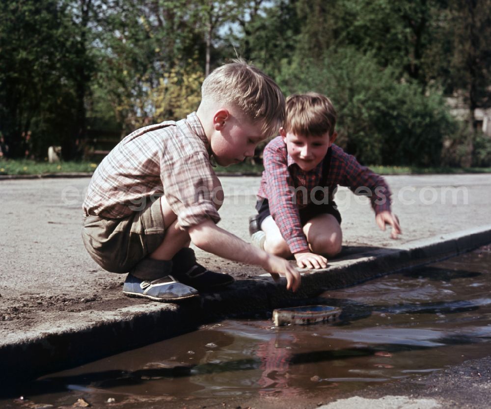 GDR picture archive: Berlin - Two boys play with a toy ship at a puddle on a street in East Berlin in the territory of the former GDR, German Democratic Republic