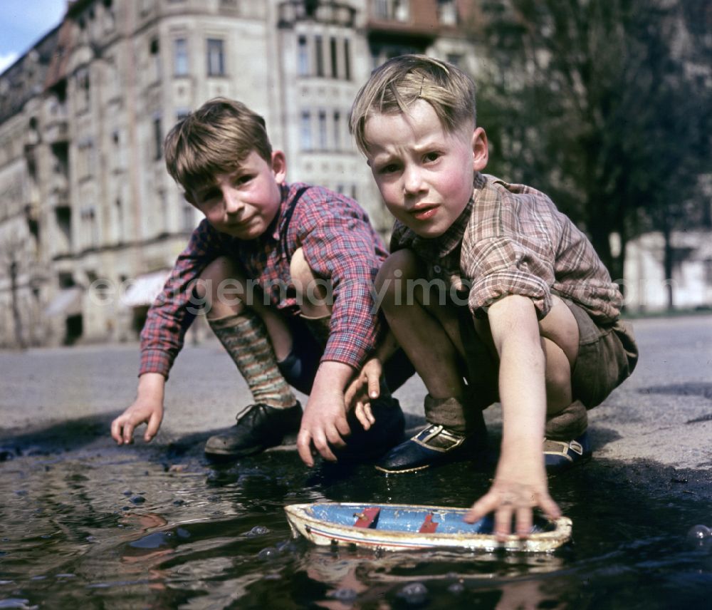 GDR image archive: Berlin - Two boys play with a toy ship at a puddle on a street in East Berlin in the territory of the former GDR, German Democratic Republic